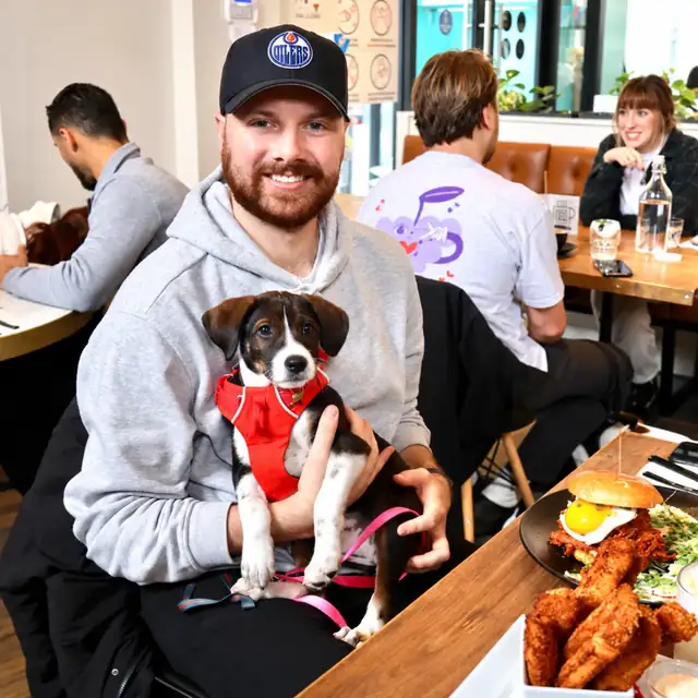 Smiling guest holding a puppy in a red harness, next to a fried chicken burger at Ruby Café MTL